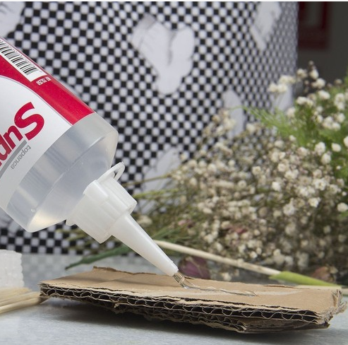 Clear craft adhesive glue being applied onto a piece of corrugated cardboard.
