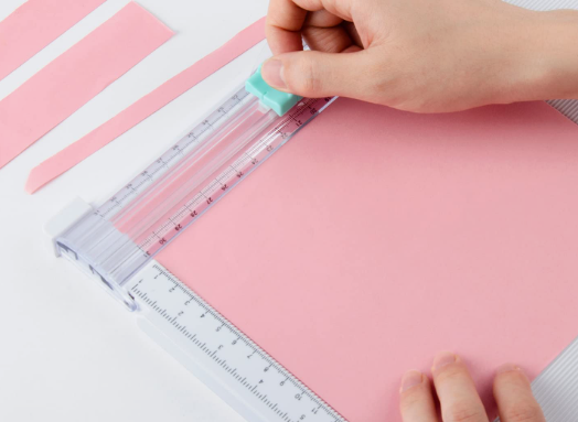 Person cutting pink paper using a precision paper trimmer craft tool.
