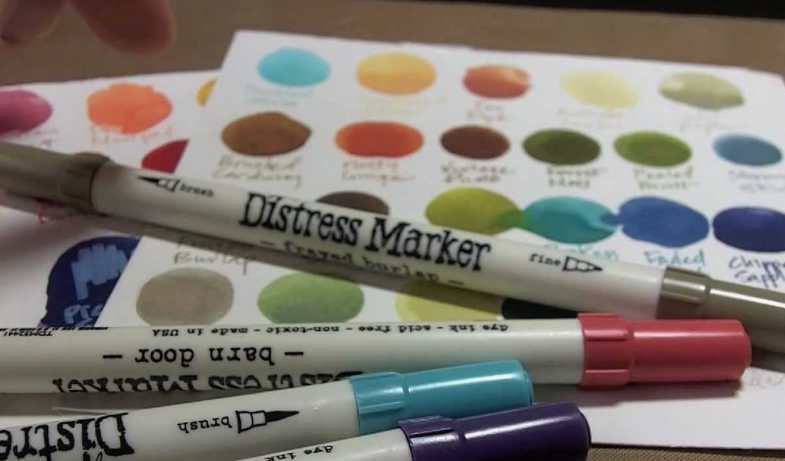 Dual-tip Distress Markers placed over a color swatch reference chart for crafting and coloring.