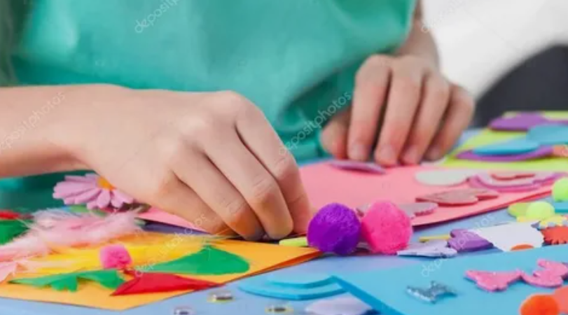 Child crafting with colorful construction paper, feathers, and pom-poms.