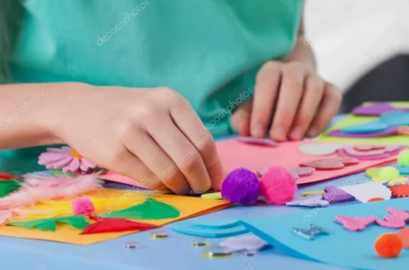Child crafting with colorful construction paper, feathers, and pom-poms.