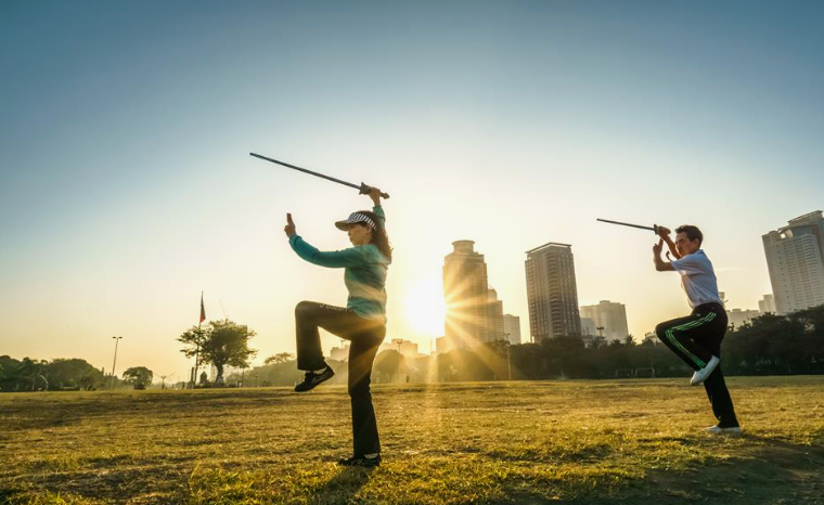 "Two people practicing tai chi with swords outdoors during sunrise, highlighting physical activity as one of the 5 pillars of wellness for strength and vitality."