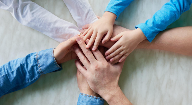 "Family members stacking their hands together, symbolizing social connection and community support as one of the 5 pillars of wellness."