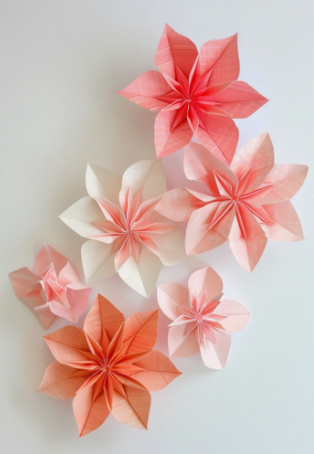 A cluster of delicate, handmade easy paper crafts featuring layered origami flowers in shades of pink, peach, and white.