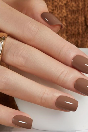 What nail colour is trending now showcased as glossy, warm coffee-brown polish on short square nails while holding a white cup.