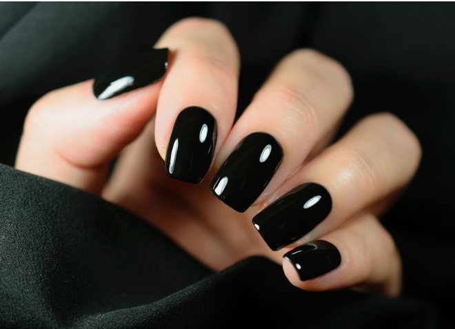 What nail colour is trending now shown as a sleek, high-gloss black polish on neat square nails against a dark fabric background.