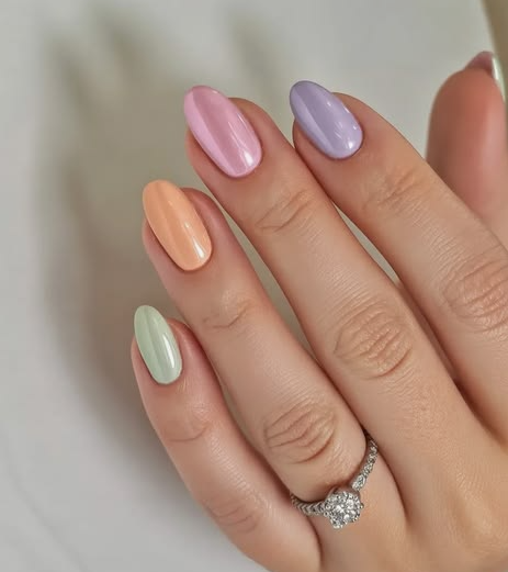 What nail colour is trending now highlighted as a multi-colored pastel skittle manicure featuring glossy mint green, peach, pink, and lavender shades on oval nails.