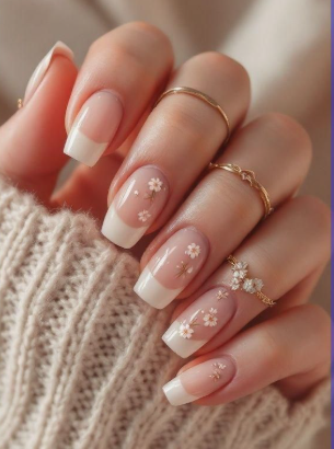 What nail colour is trending now styled as a classic French manicure with white tips and delicate floral nail art accents on square nails, worn with gold rings.