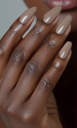 A close-up of dark-skinned hands featuring glossy neutral brown almond-shaped nails in a guide on nail colors that age your hands.