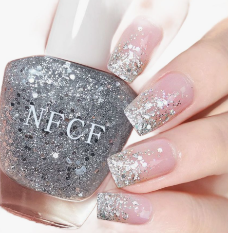 A hand holding an NFCF silver glitter nail polish bottle with square nails featuring a silver sparkle gradient, demonstrating nail colors that age your hands.