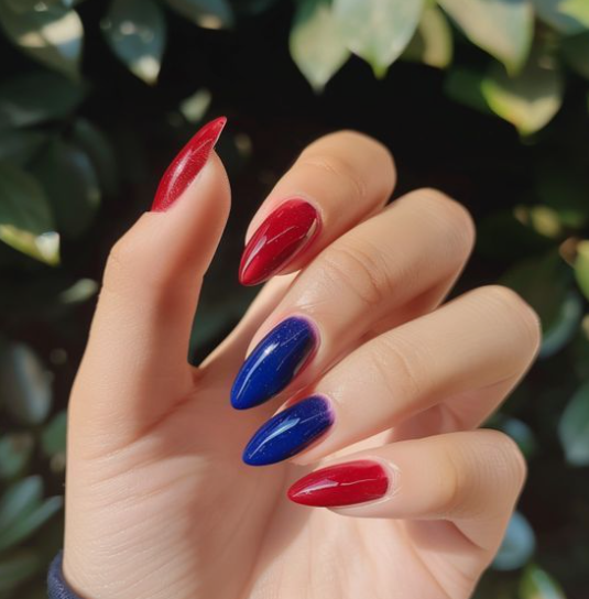 A hand with almond-shaped nails featuring alternating red and deep blue polish in an article covering nail colors that age your hands.