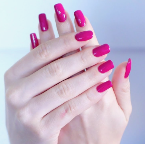 A pair of hands with short, square-shaped fingernails painted in a vibrant, glossy magenta or bright pink nail polish.
