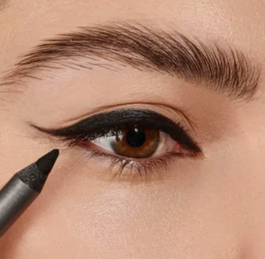 10 Makeup Trends for 2026: The Beauty Looks Everyone Will Want to Try A close-up of a model applying black eyeliner with a pencil to create a defined wing, showcasing makeup trends 2026 alongside fluffy, laminated eyebrows.