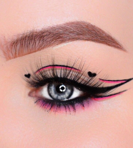 10 Makeup Trends for 2026: The Beauty Looks Everyone Will Want to Try A close-up of creative graphic eye makeup showcasing makeup trends 2026, featuring sharp black winged eyeliner layered with vibrant pink accent lines, delicate heart motifs at the corners, fluffy lashes, and neatly groomed brows.