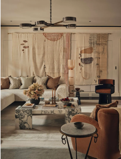 Contemporary living room embodying interior design trends 2026, featuring a marble coffee table, textured wall hangings, and a mix of warm earth tones.