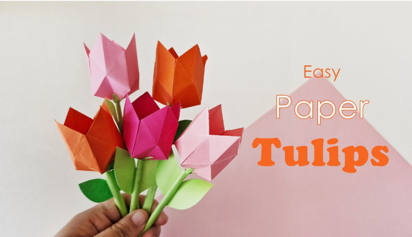 15 Easy DIY Paper Flowers for Kids: Fun Crafts for Toddlers, Preschoolers & Older Children A hand holding a small bouquet of folded origami paper tulips in orange, pink, and red with green stems and leaves, styled as easy paper flowers for kids.