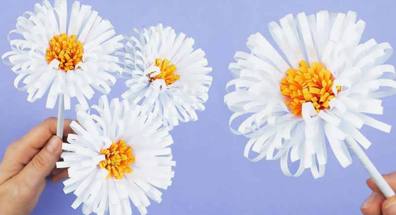 15 Easy DIY Paper Flowers for Kids: Fun Crafts for Toddlers, Preschoolers & Older Children Several handmade white paper chrysanthemum flowers with detailed orange and yellow fringed centers and white stems, featured as easy paper flowers for kids.
