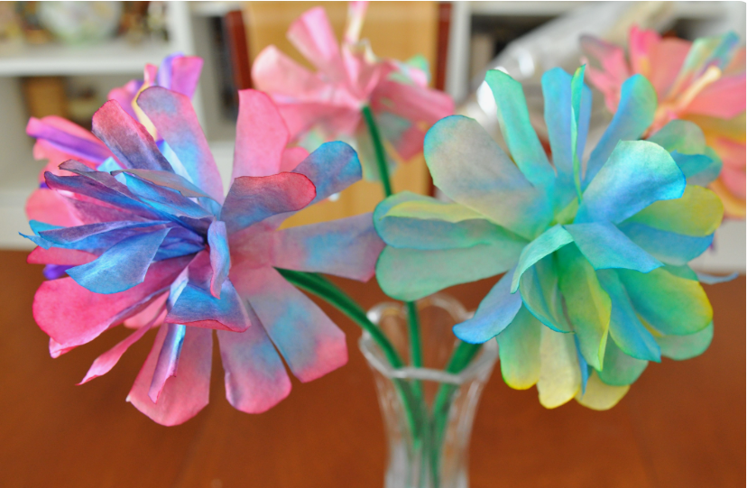 15 Easy DIY Paper Flowers for Kids: Fun Crafts for Toddlers, Preschoolers & Older Children A bouquet of vibrant tie-dye coffee filter flowers in shades of pink, blue, yellow, and green on green stems arranged in a glass vase, showcased as easy paper flowers for kids.