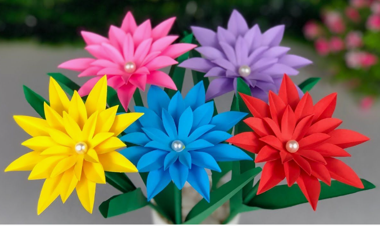 15 Easy DIY Paper Flowers for Kids: Fun Crafts for Toddlers, Preschoolers & Older Children A bouquet of vibrant multi-layered paper flowers in yellow, pink, blue, purple, and red, each featuring a pearl bead center and mounted on green stems with leaves, presented as easy paper flowers for kids.