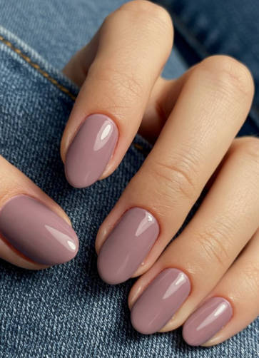 25 Short Fall Nail Ideas for 2026: Chic, Simple & Trendy Designs Short fall nail ideas 2026 showcasing short, oval nails finished in a glossy dusty mauve-pink polish against denim.