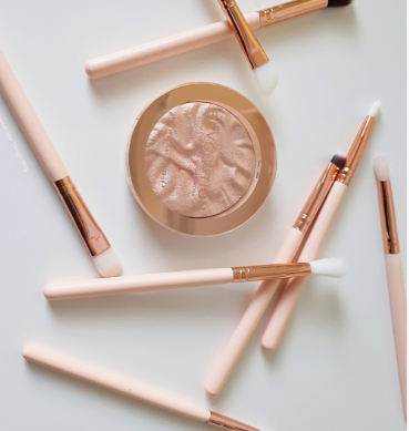 20 Types of Makeup and Their Uses: A Complete Beginner’s Guide Makeup highlighter compact surrounded by rose gold makeup brushes for types of makeup and their uses.