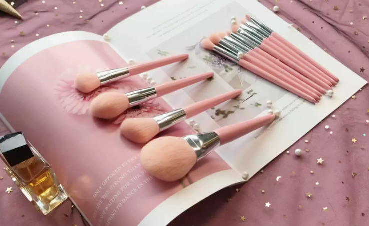 20 Types of Makeup and Their Uses: A Complete Beginner’s Guide Set of pink makeup brushes with pearl accents resting on an open magazine for types of makeup and their uses.