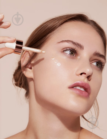 20 Types of Makeup and Their Uses: A Complete Beginner’s Guide Woman applying liquid highlighter drops with a dropper onto her cheekbone for types of makeup and their uses.