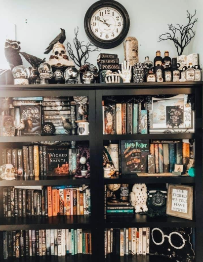 A tall black bookcase topped with potion bottles, skull figurines, a crow, and a vintage clock, embodying Halloween decor ideas for indoor spaces.
