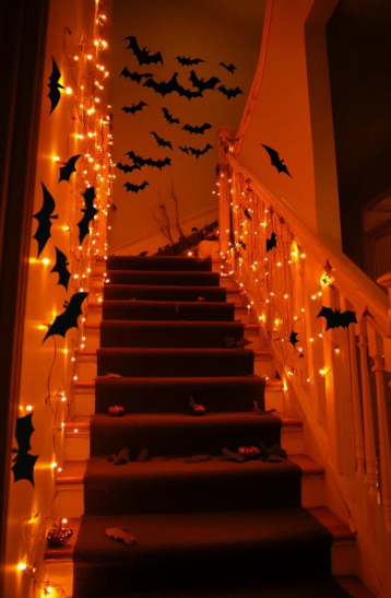 Cascading vertical strings of warm orange fairy lights illuminating the staircase walls, showcasing vibrant Halloween decor ideas for indoor spaces.