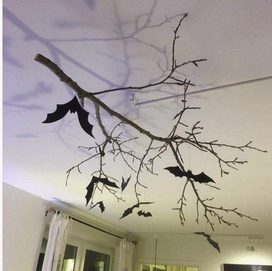 : A large, natural bare branch hung horizontally from a plain white ceiling, creating a rustic and striking focal point for Halloween decor ideas for indoor spaces.