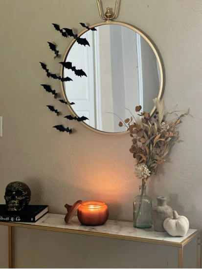 A round gold-framed mirror mounted on a neutral wall, beautifully accented with a cascading swarm of black paper bats curving along the side, highlighting Halloween decor ideas for indoor spaces.
