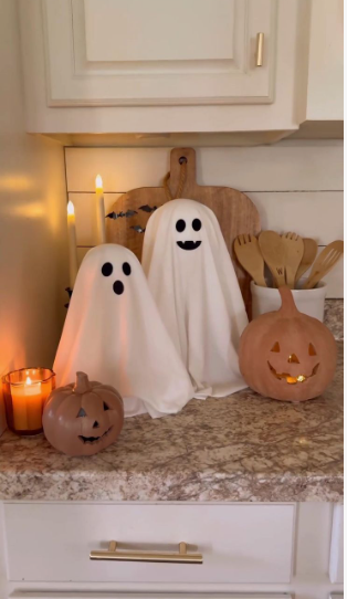 A cozy kitchen counter corner featuring two handmade fabric ghost figures paired with carved pumpkins and candles as charming Halloween decor ideas for indoor spaces.