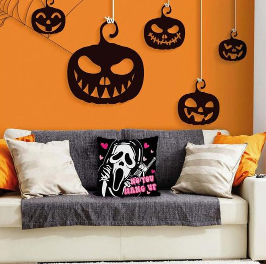Black felt or cardboard jack-o'-lantern silhouettes suspended at varying heights against a vibrant orange wall, showcasing playful Halloween decor ideas for indoor spaces.