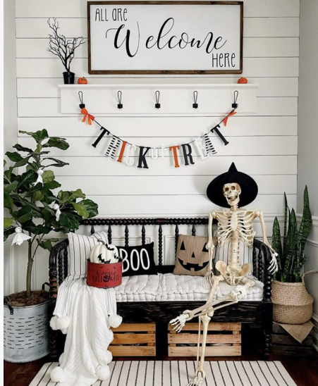A decorative skeleton wearing a witch hat seated on a black spindle bench laden with throw pillows, showcasing creative Halloween decor ideas for indoor spaces.
