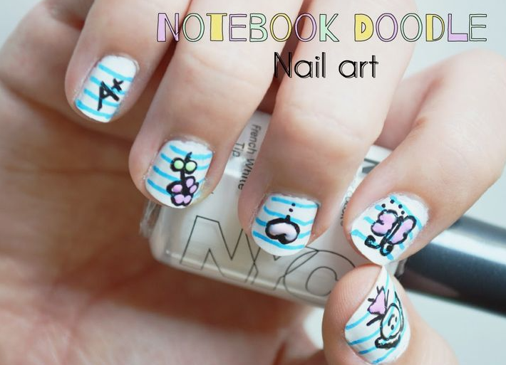 18 Back-to-School Nail Designs for a Fresh Start This School Year Close-up of playful back-to-school nail designs featuring a notebook paper background pattern with cute doodle art including an A-plus grade, flowers, and sketches.