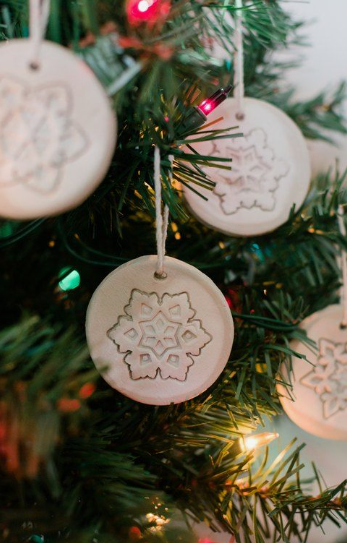 Handmade air dry clay ideas hanging on a Christmas tree, showcasing round white clay ornaments with intricate carved snowflake designs.