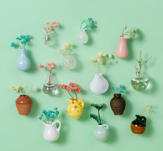 A flat lay showcasing creative air dry clay ideas featuring various miniature vases filled with tiny dried flowers against a green background.