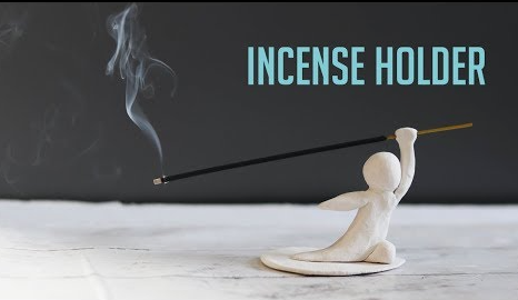 A white clay sculpture shaped like a small figure holding an incense stick, highlighting creative air dry clay ideas for home decor.