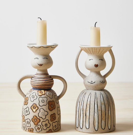 Two whimsical candlestick holders showcasing unique air dry clay ideas, styled as human figures with floral and striped dresses holding lit candles.