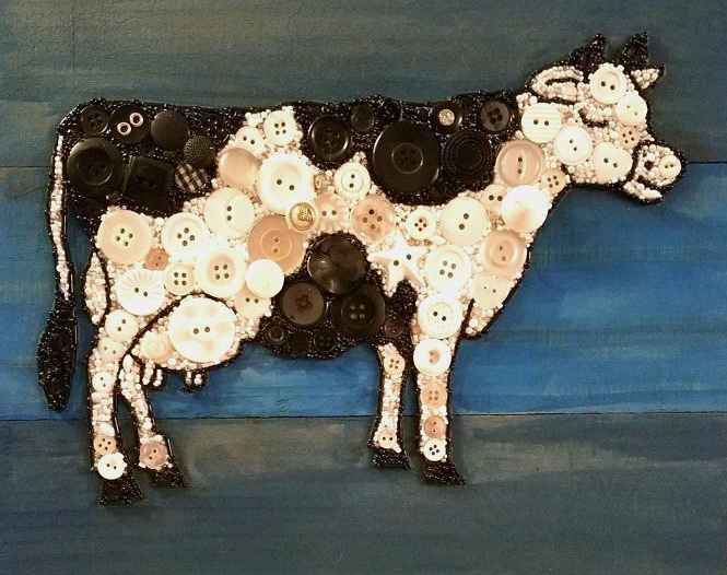 30 Creative DIY Button Crafts to Turn Spare Buttons Into Beautiful Decor A detailed wall art piece featuring a standing cow silhouette filled with a patchwork of black, white, and translucent buttons against a dark wooden background, highlighting DIY button crafts.