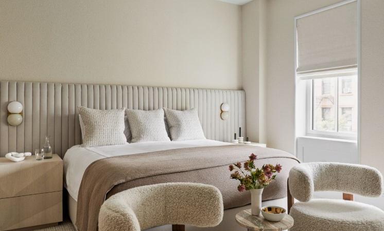 Small Living Room Decor Ideas on a Budget: 25 Stylish Ways to Make It Look Expensive Cozy neutral bedroom featuring small living room decor ideas on a budget with an upholstered channel-tufted headboard, textured accent pillows, a brown throw blanket, matching nightstands, modern wall sconces, and bouclé armchairs around a small side table.