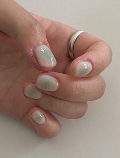 Short nail designs featuring an ethereal green aura gradient effect accented with tiny white star sparkles on a glossy neutral base.