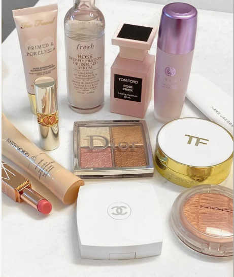 Flat lay of luxury beauty products worth buying, including designer makeup palettes, high-end skincare serums, and luxury perfumes arranged on a white marble surface.