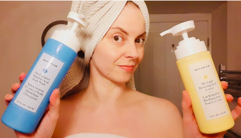 Woman wrapped in a towel holding up Naturium body wash and lotion, showcasing beauty products worth buying.