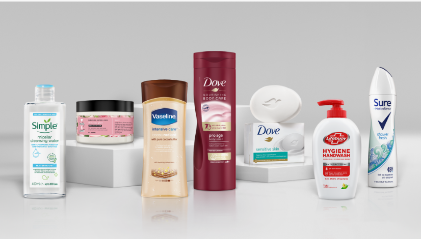 Flat lay of popular personal care products worth buying featuring an assortment of skincare and hygiene essentials from brands like Simple, Vaseline, Dove, Lifebuoy, and Sure arranged on white platforms against a neutral background.