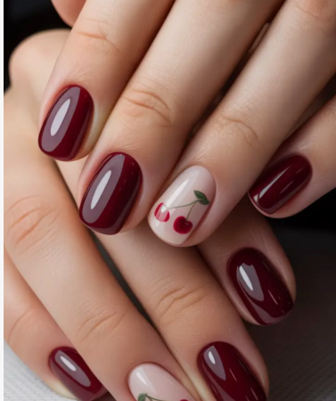 A close-up of hands displaying a manicure with short, rounded nails painted in a glossy deep maroon or burgundy polish, featuring a nude accent nail on each hand decorated with tiny red cherry illustrations with green stems.