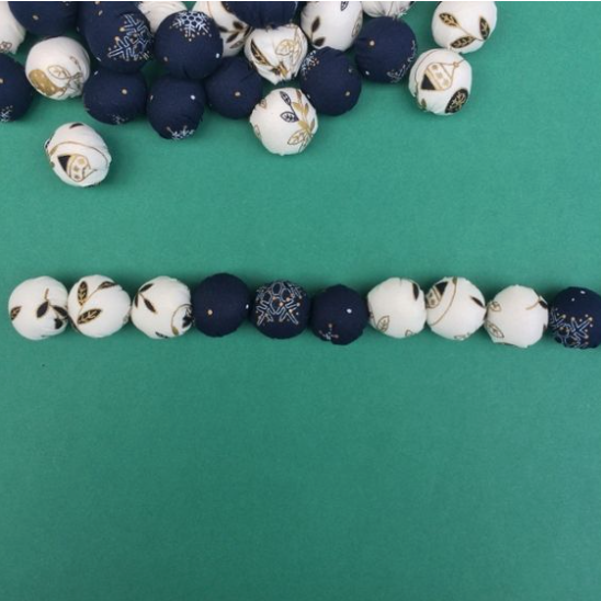A collection of small round beads covered in navy blue and white fabric with festive gold patterns, shown arranged in a row and scattered on a green background, showcasing cheap DIY crafts on a budget.