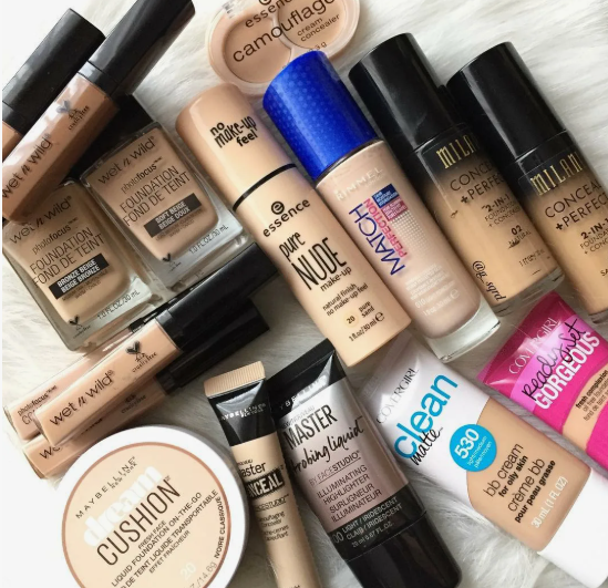 Flat lay arrangement of various affordable foundation, concealer, and BB cream tubes from brands like Wet n Wild, Milani, and CoverGirl, highlighting best drugstore beauty products under $20.