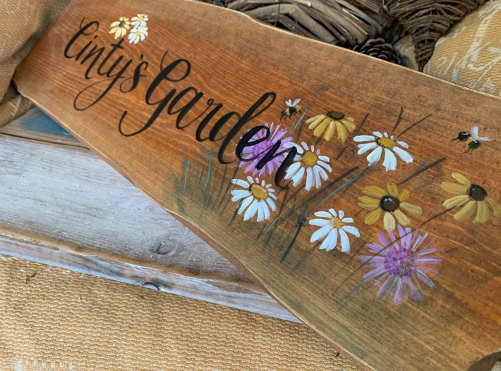 A rustic wooden sign hand-painted with daisies, bees, and the custom text "Cinty's Garden," demonstrating inspiring home decor ideas without buying anything.