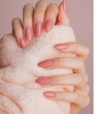 Hands holding a soft pink fluffy blanket, showcasing polished almond-shaped dusty rose nails as graceful nail colors that make hands look younger.